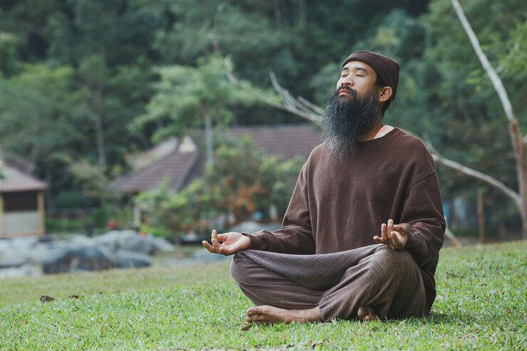 An Asian man meditating on green grass