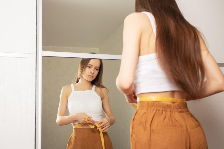 Teenager measuring her waist in front of a mirror