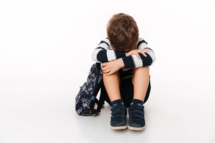 child seated down with gloomy face, school bag by his side